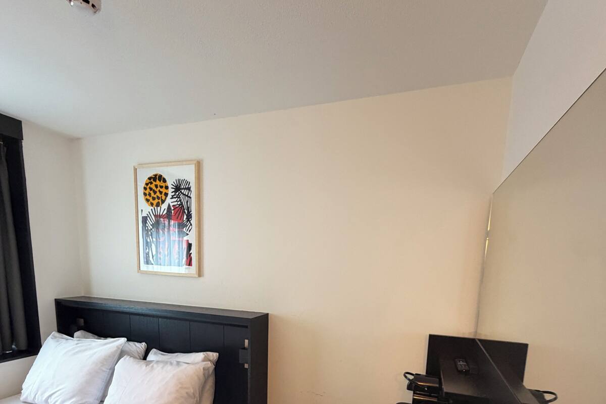 Une chambre d’hôtel équipée d’un lit, d’un bureau, d’une chaise, d’une lampe de bureau, d’un téléphone et d’un tableau encadré au mur.