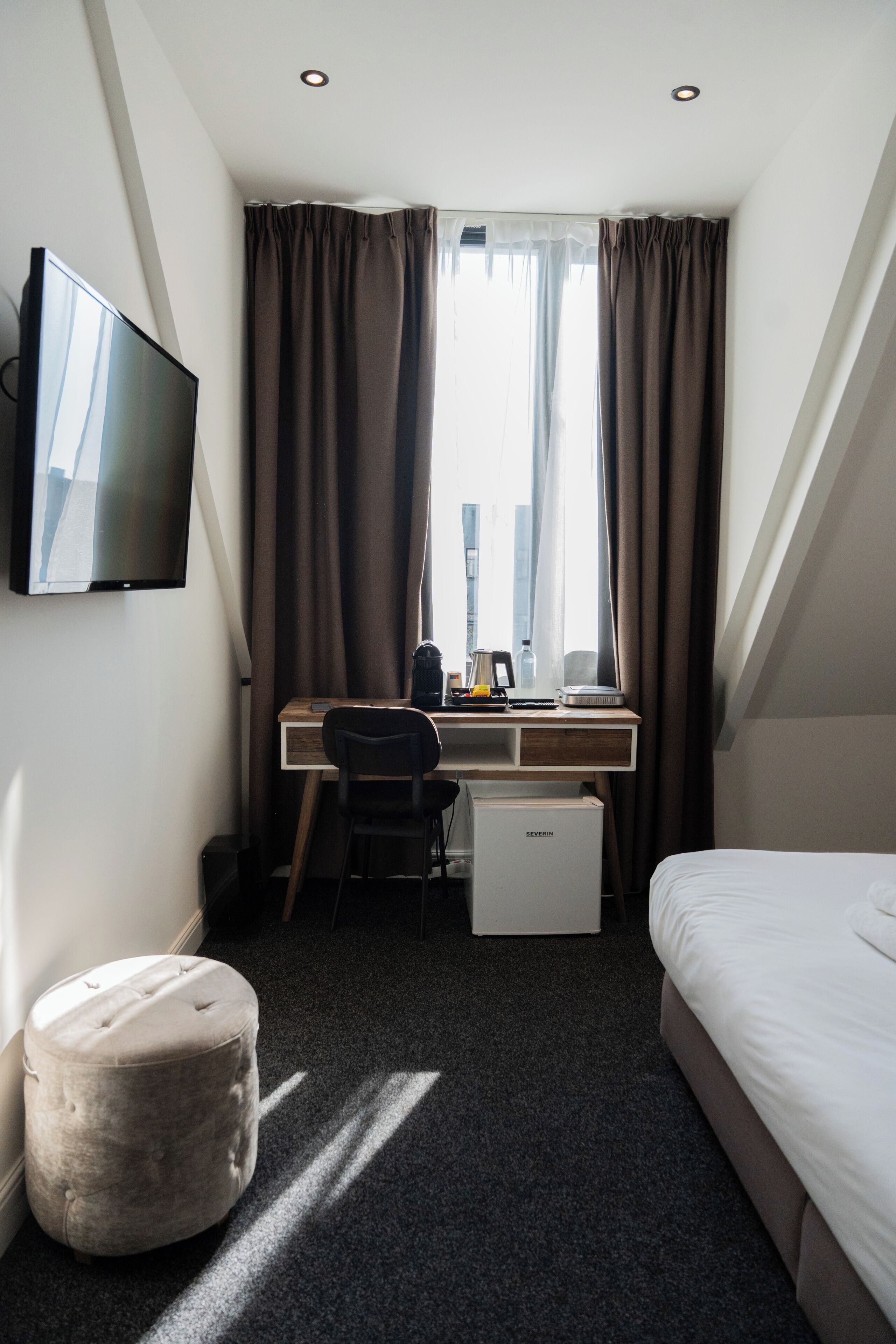 Habitación de hotel con cama, escritorio, silla, televisor y ventana con cortinas.