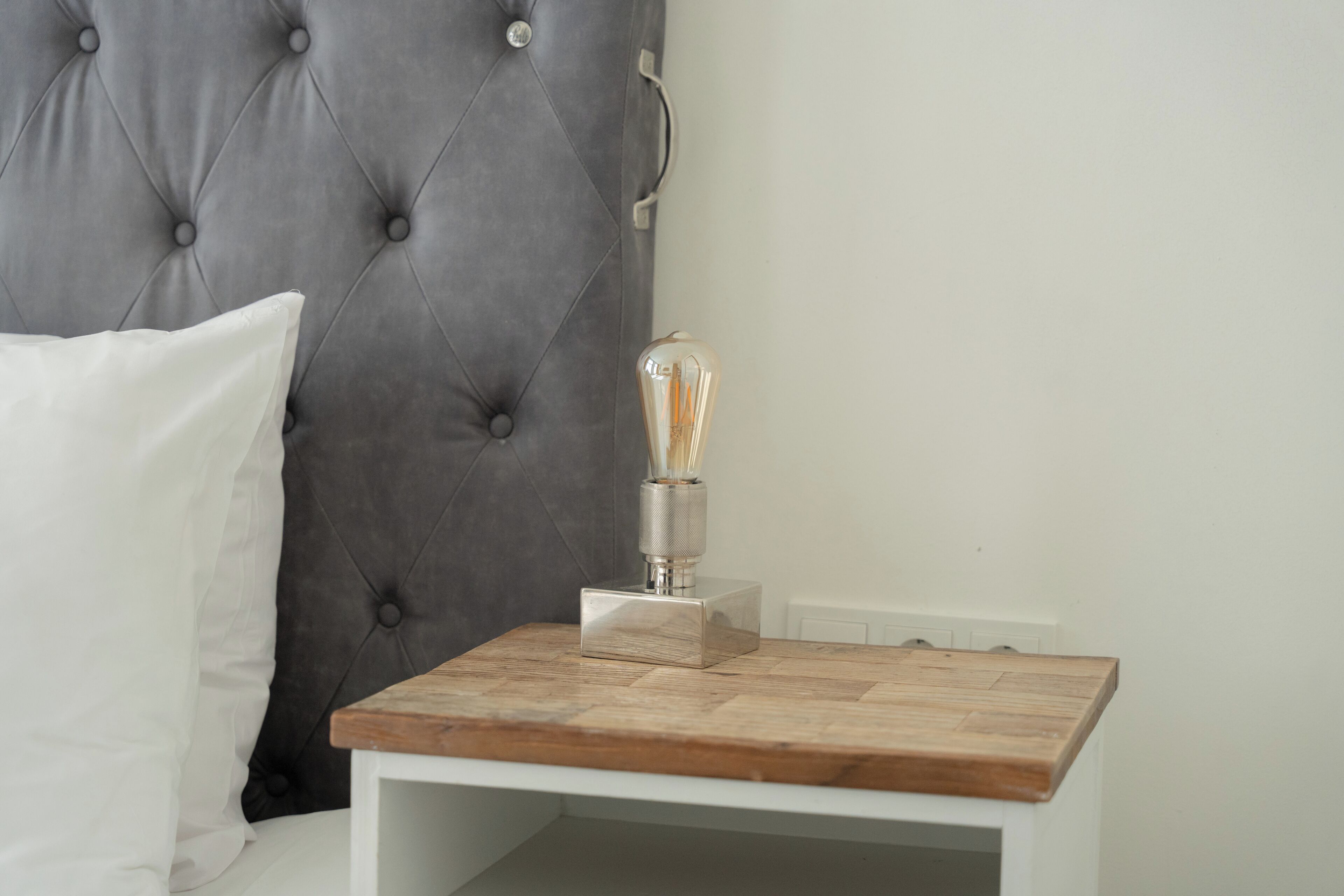 Cabecera con textura, mesita de noche con lámpara y almohada blanca.
