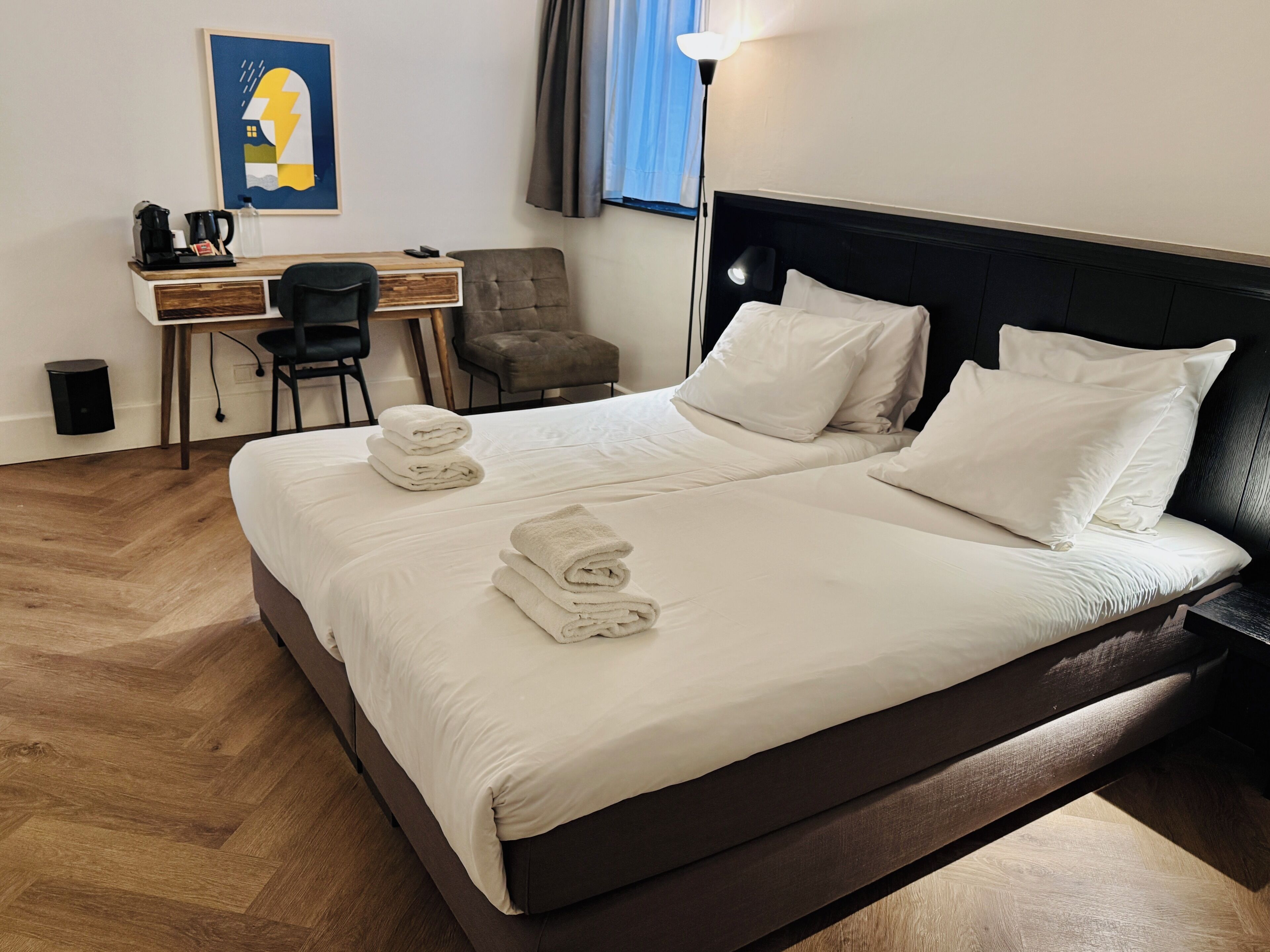 Quarto de hotel com cama, escrivaninha, cadeira e abajur.