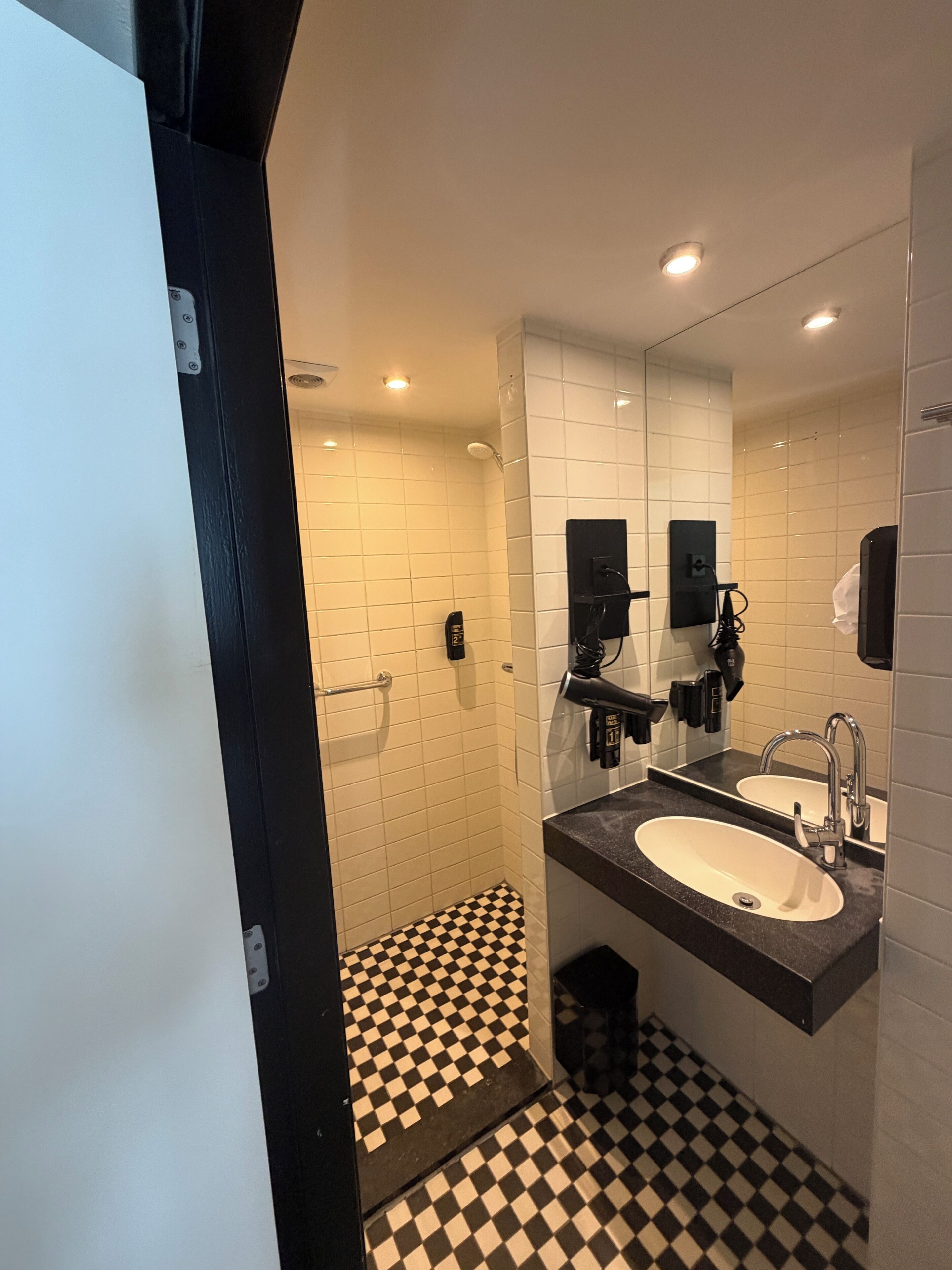 Une salle de bain moderne avec un carrelage à motifs géométriques, un grand miroir, deux lavabos et un espace douche.