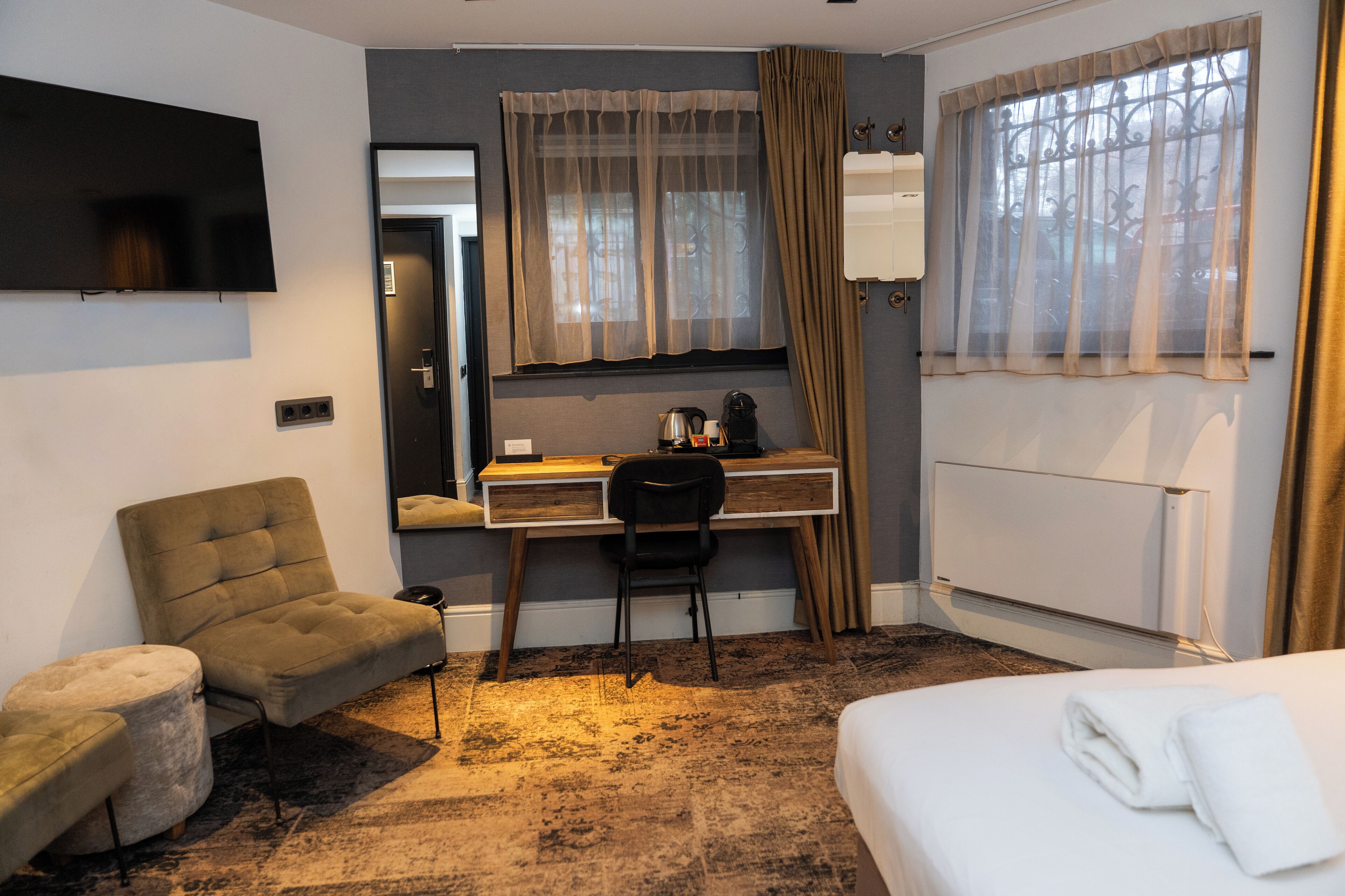 Ein Hotelzimmer mit Bett, Schreibtisch, Stuhl, Fernseher und einem Fenster mit Vorhängen.