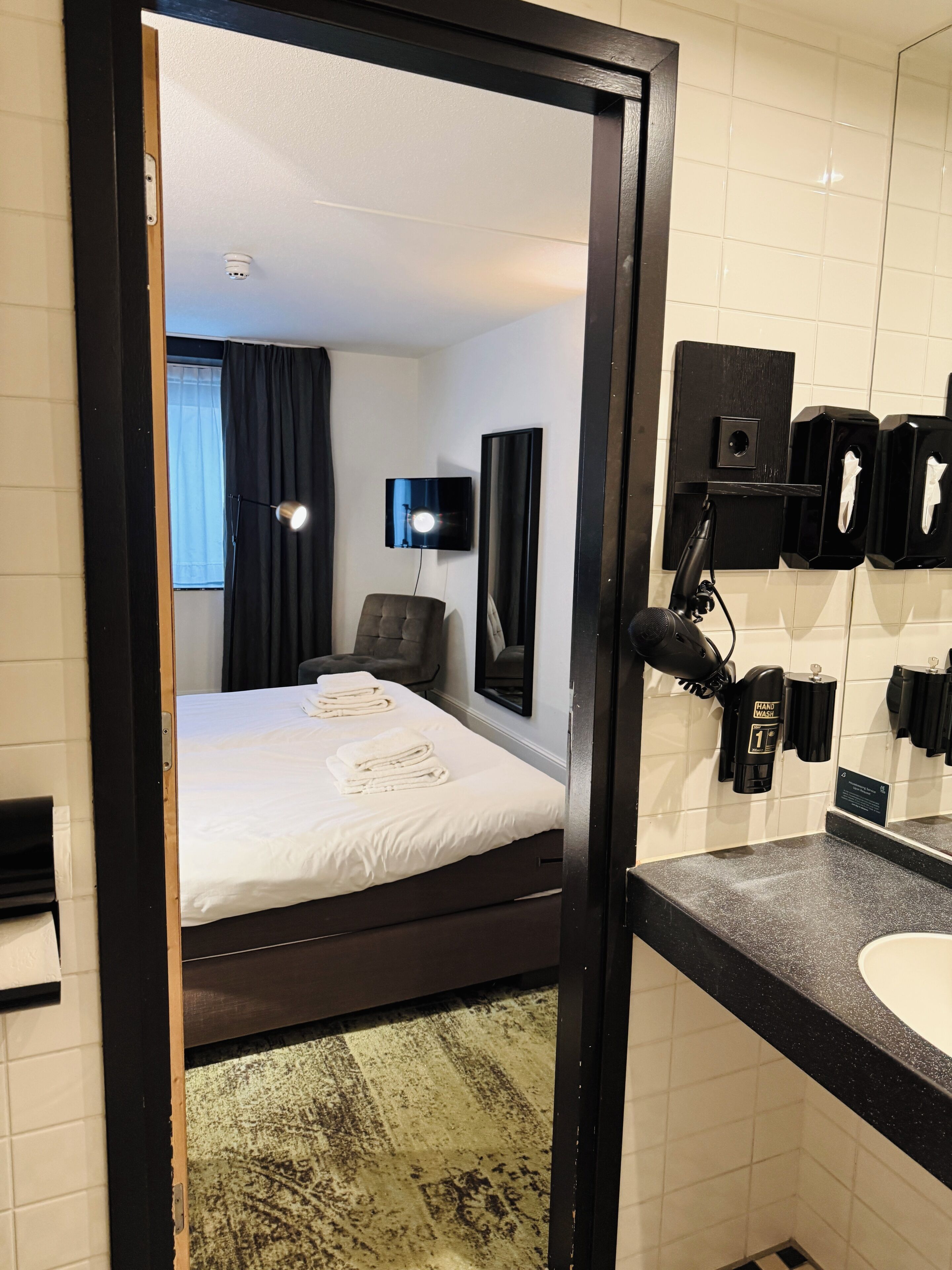 Ein Hotelzimmer mit Bett, Schreibtisch, Stuhl, Schreibtischlampe, Fernseher, Handtrockner und Spiegel.
