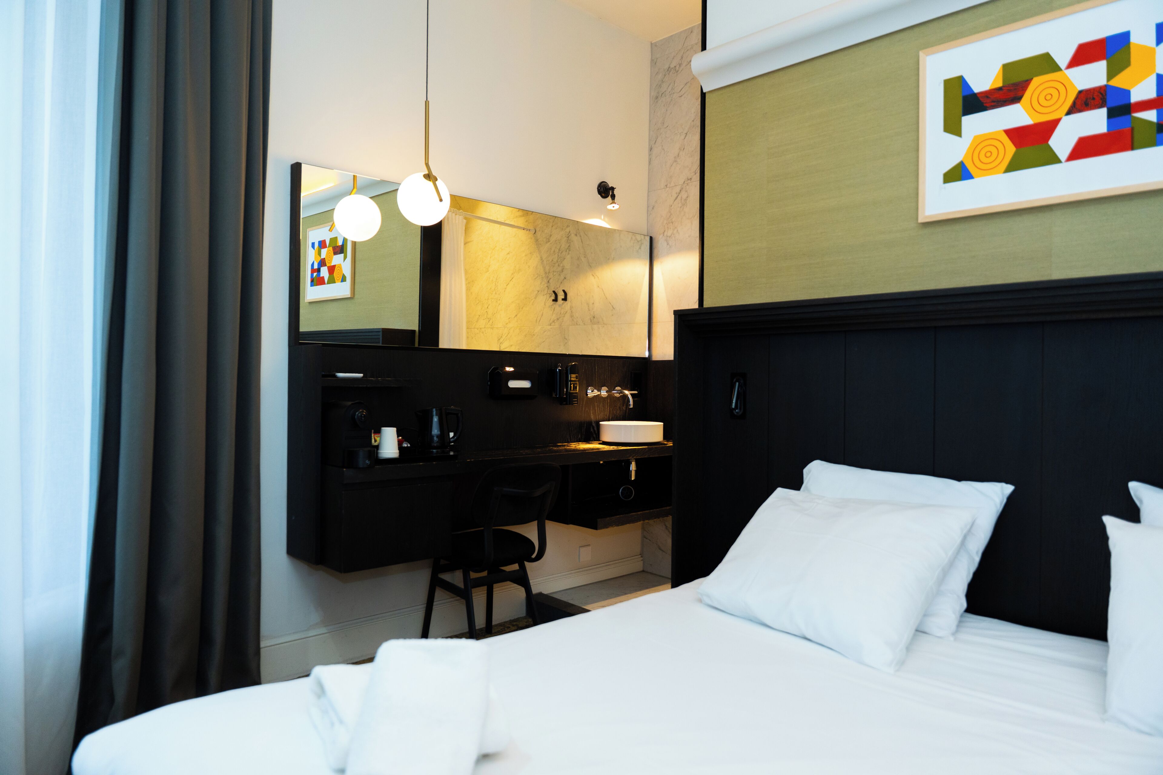 Quarto de hotel com cama, escrivaninha, cadeira, espelho e um quadro na parede.