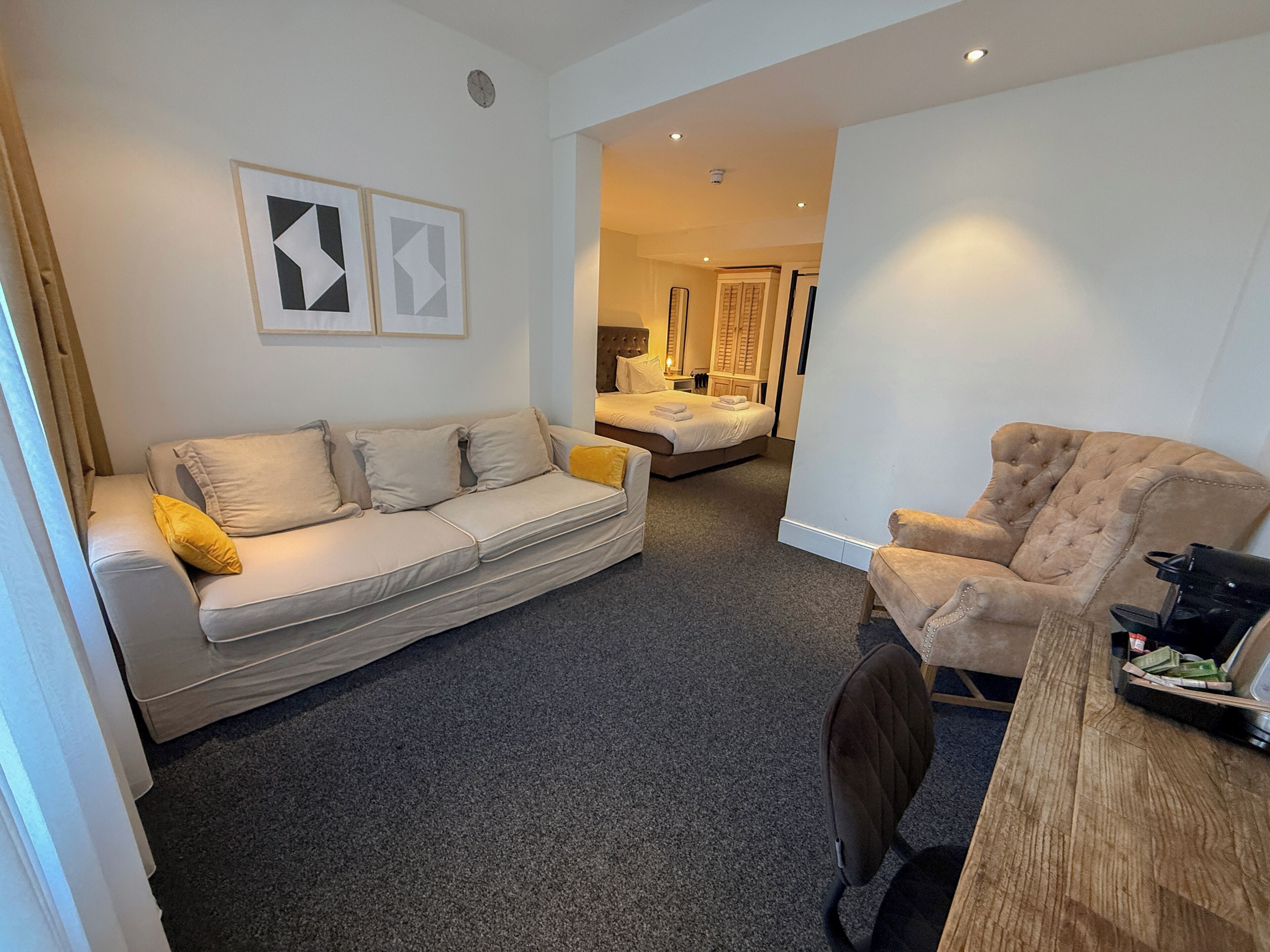 A modern hotel room with a sofa, armchair, and a dining table.