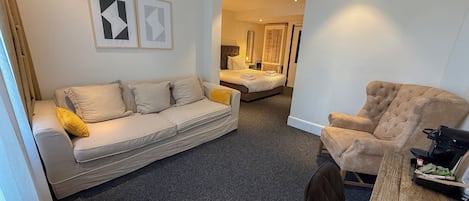 Una habitación de hotel moderna con sofá, sillón y una mesa de comedor.