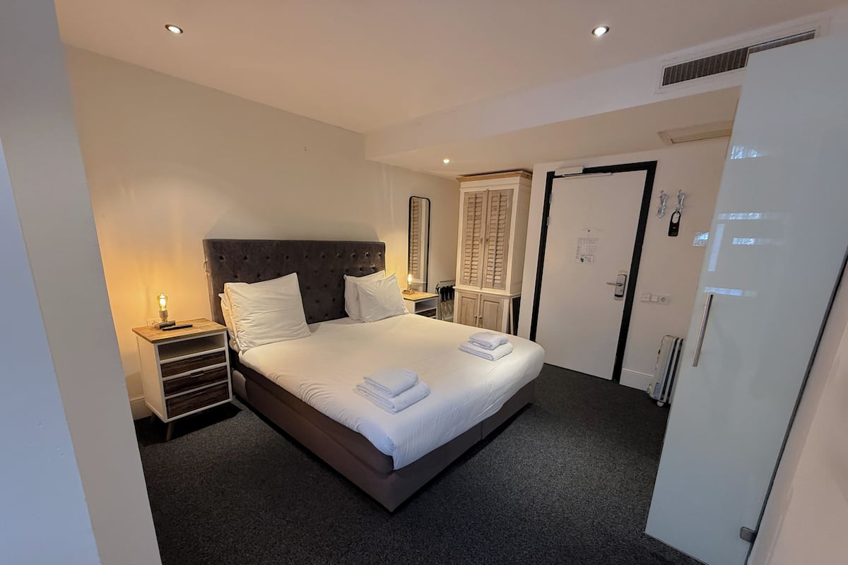 Une chambre d’hôtel avec un grand lit, des tables de chevet, une armoire et une porte dotée d’une poignée.