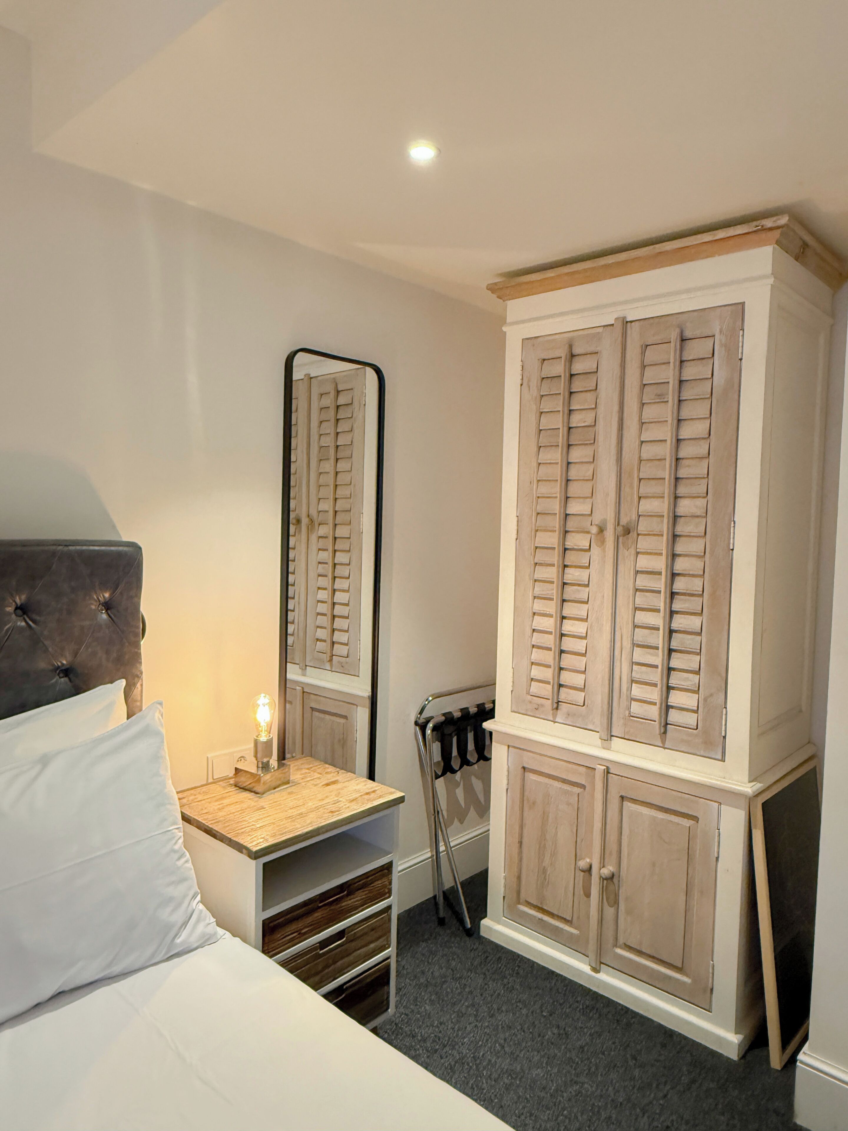 Een slaapkamer met een bed, nachtkastje, dressoir, spiegel en radiator.