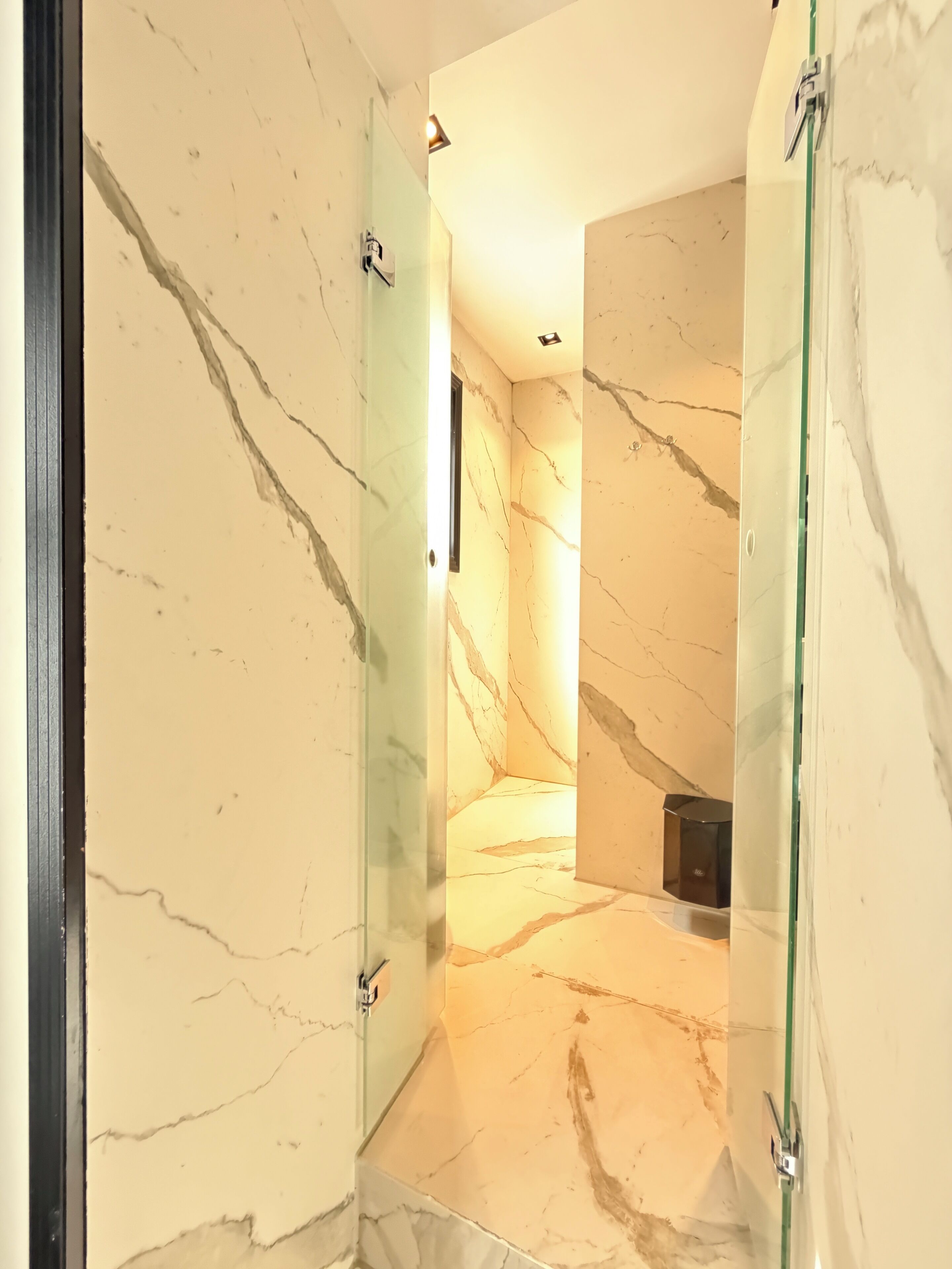 Un baño moderno con paredes de mármol y cabina de ducha de vidrio.