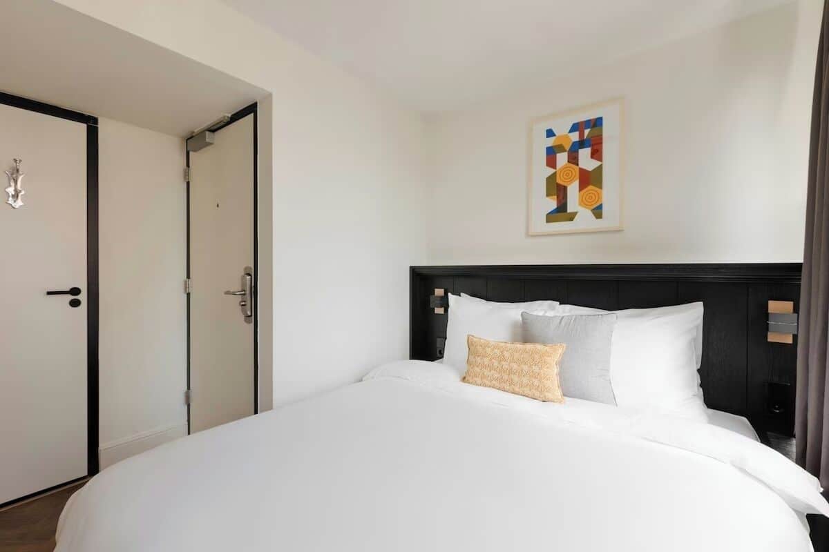 Une chambre d’hôtel avec un grand lit, une tête de lit, une porte et une œuvre d’art accrochée au mur.