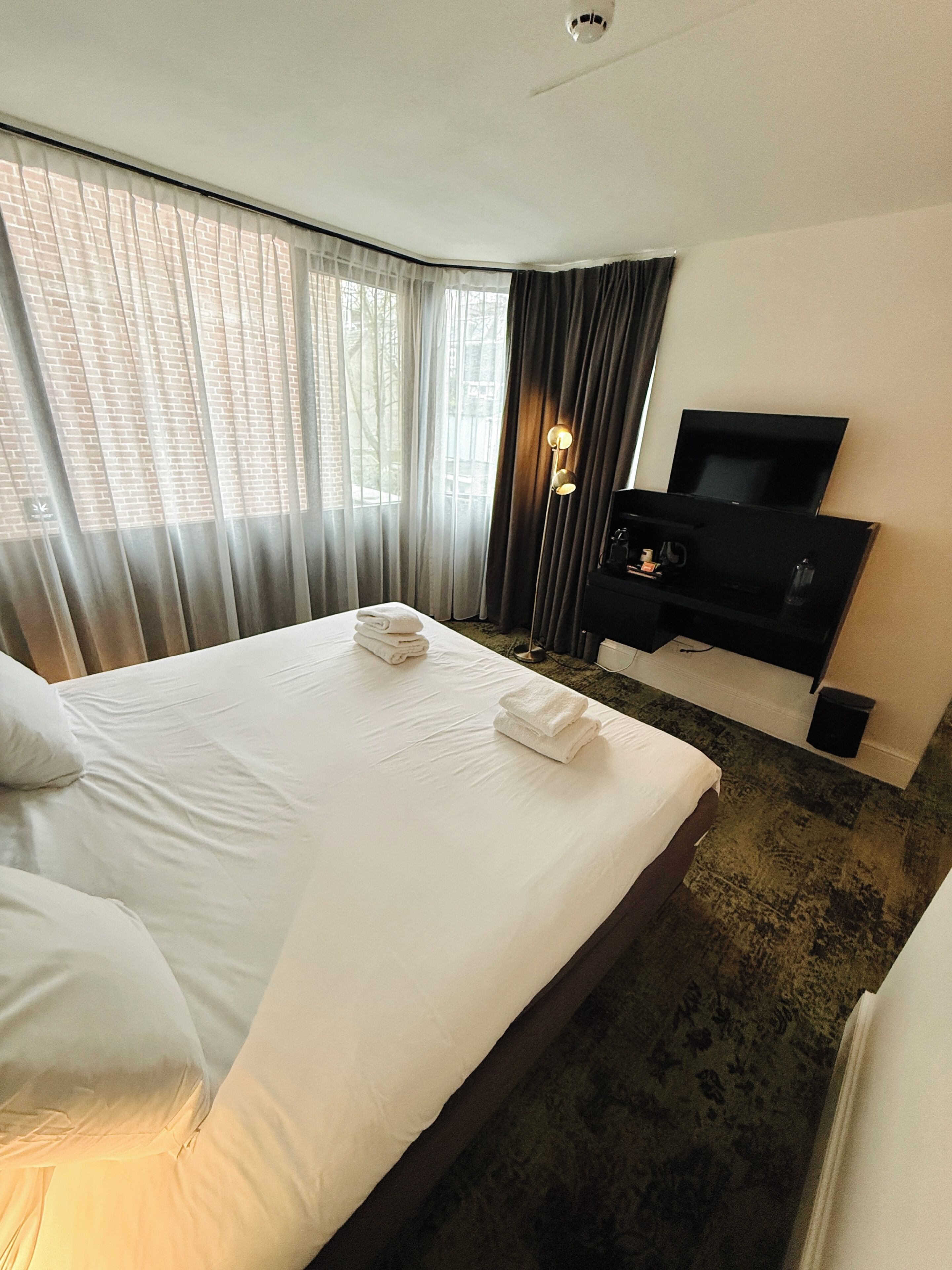 A hotel room with a large bed, a flat-screen TV, a desk, and a window with curtains.