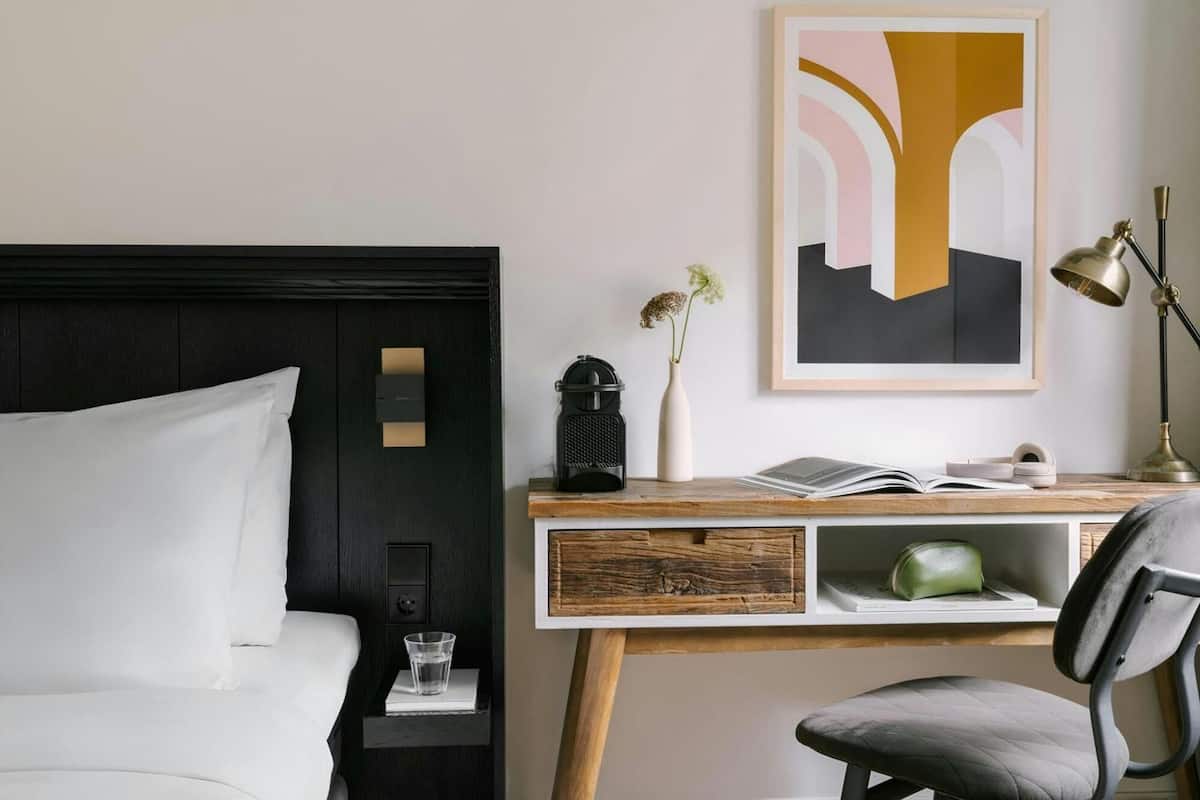 Une chambre d’hôtel avec un lit, un bureau doté d’une lampe, une chaise et un tableau abstrait encadré.