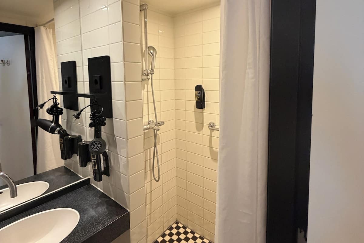 Une salle de bain avec un lavabo sur un plan de toilette noir, une douche avec un carrelage à motifs à carreaux et un rideau blanc.