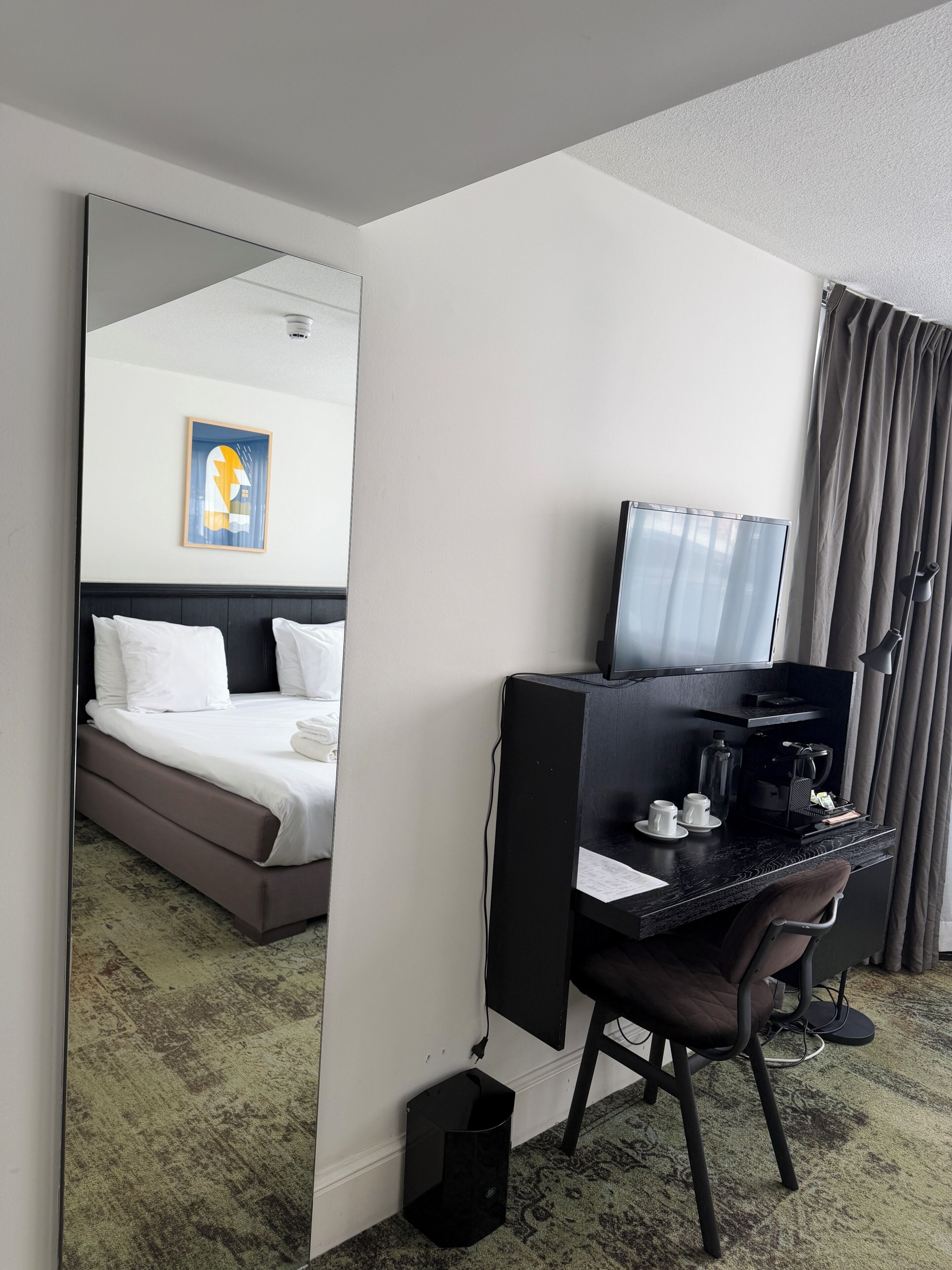 A hotel room with a bed, a desk with a computer, a mirror, a television, and a coffee maker.