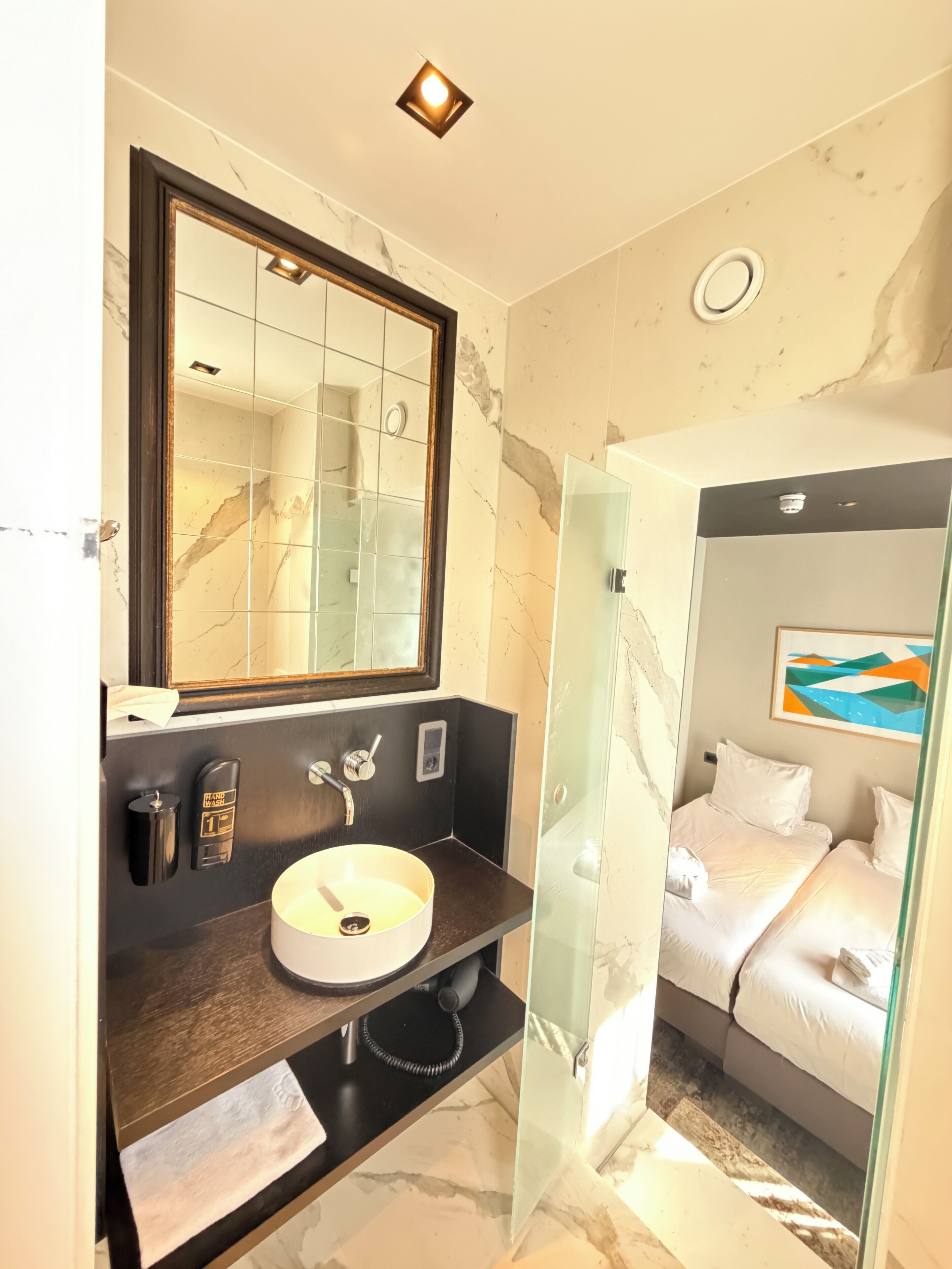 Un baño con lavamanos de mármol, secamanos automático, espejo y cabina de ducha de vidrio.