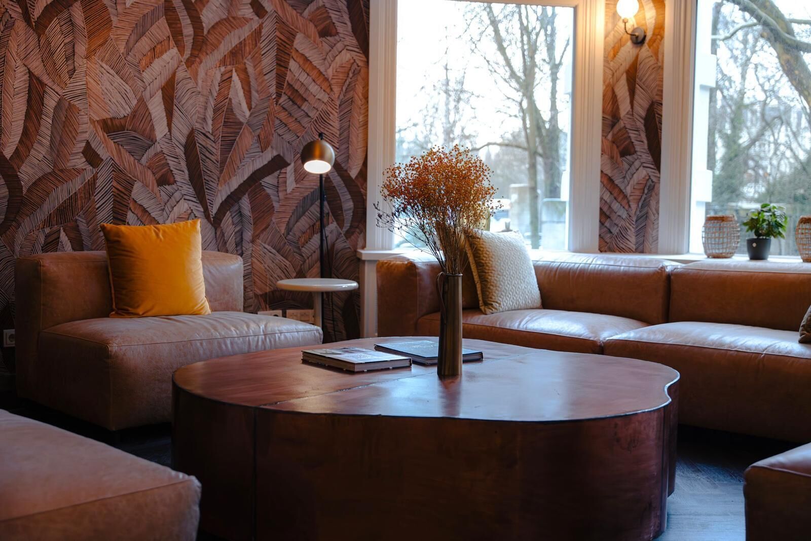 A modern living room with a patterned wall, leather sofas, a round coffee table, and a vase with dried flowers.