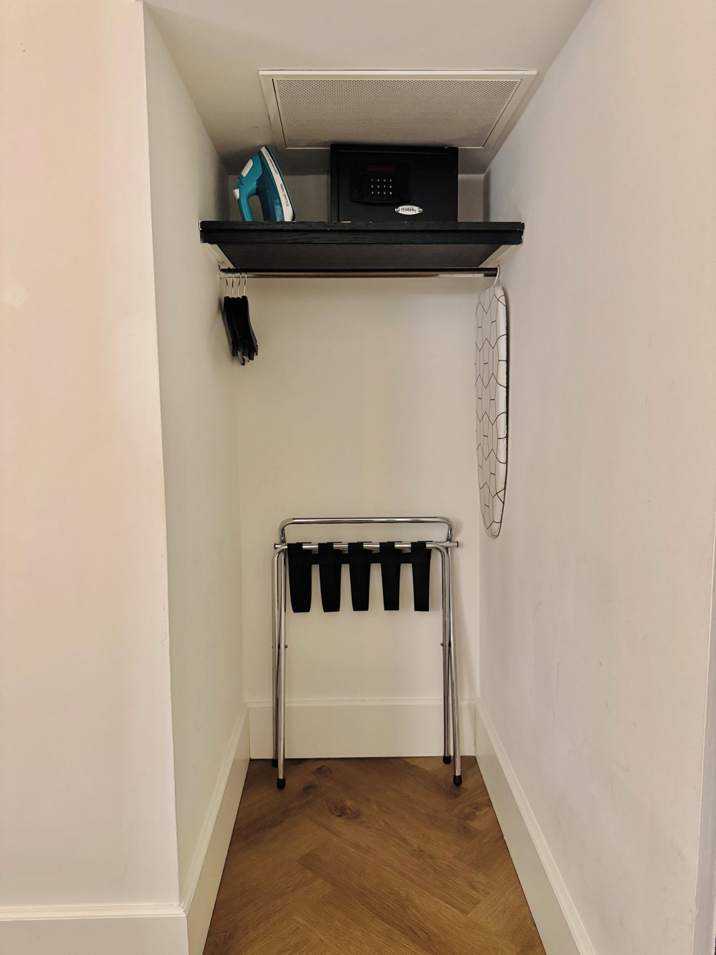 Een kleine, afgesloten ruimte met een ingebouwde verwarming, een plank met een apparaat en een metalen rek met zwarte spullen.