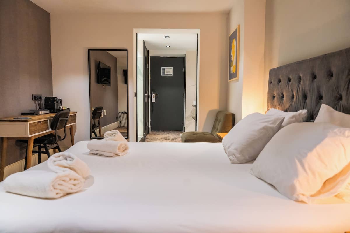 Une chambre d’hôtel comprenant un lit, un bureau avec un ordinateur, une chaise et une porte donnant sur une autre pièce.