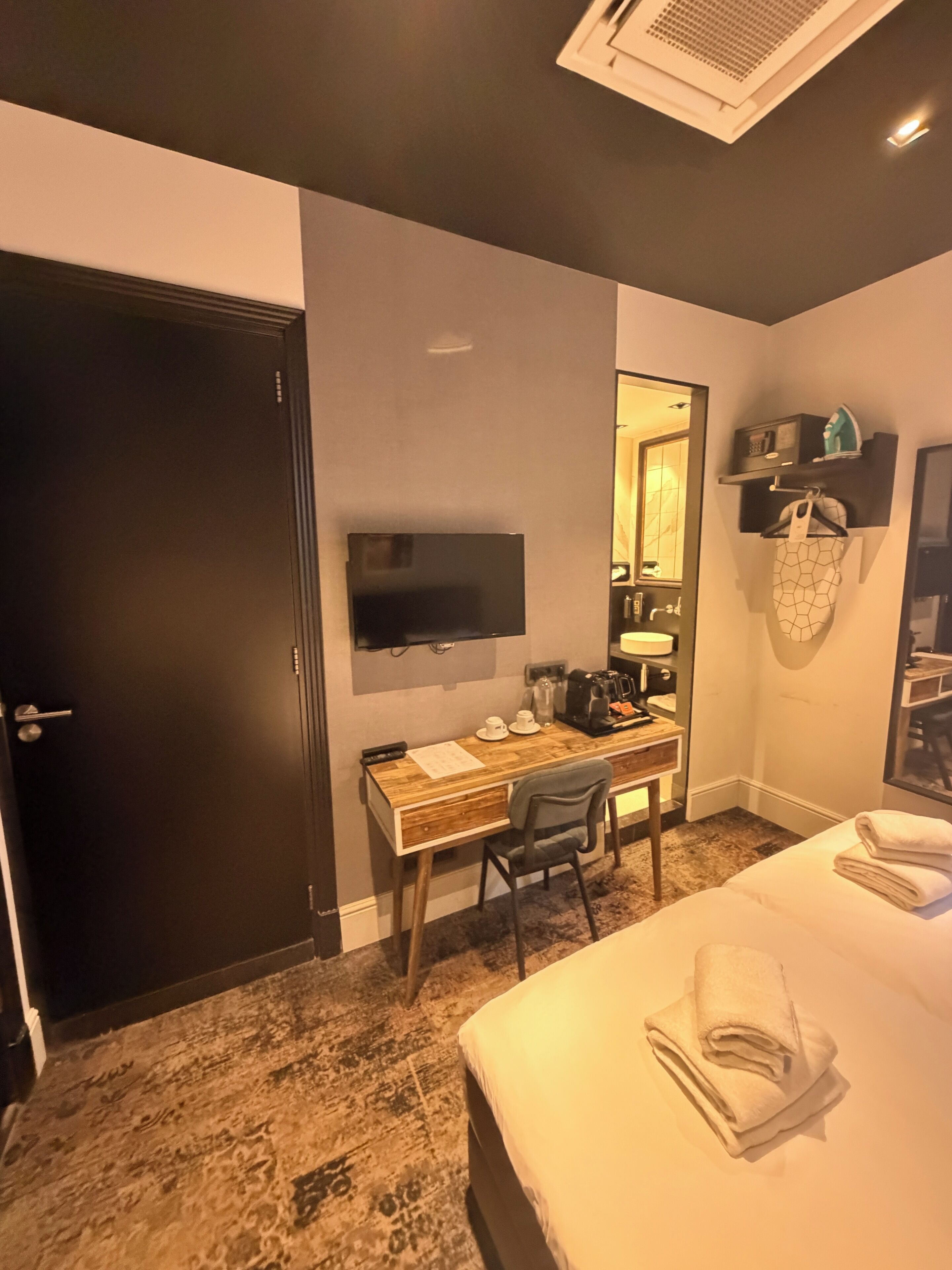 A hotel room with a bed, a desk with a chair, a television, and a mirror.
