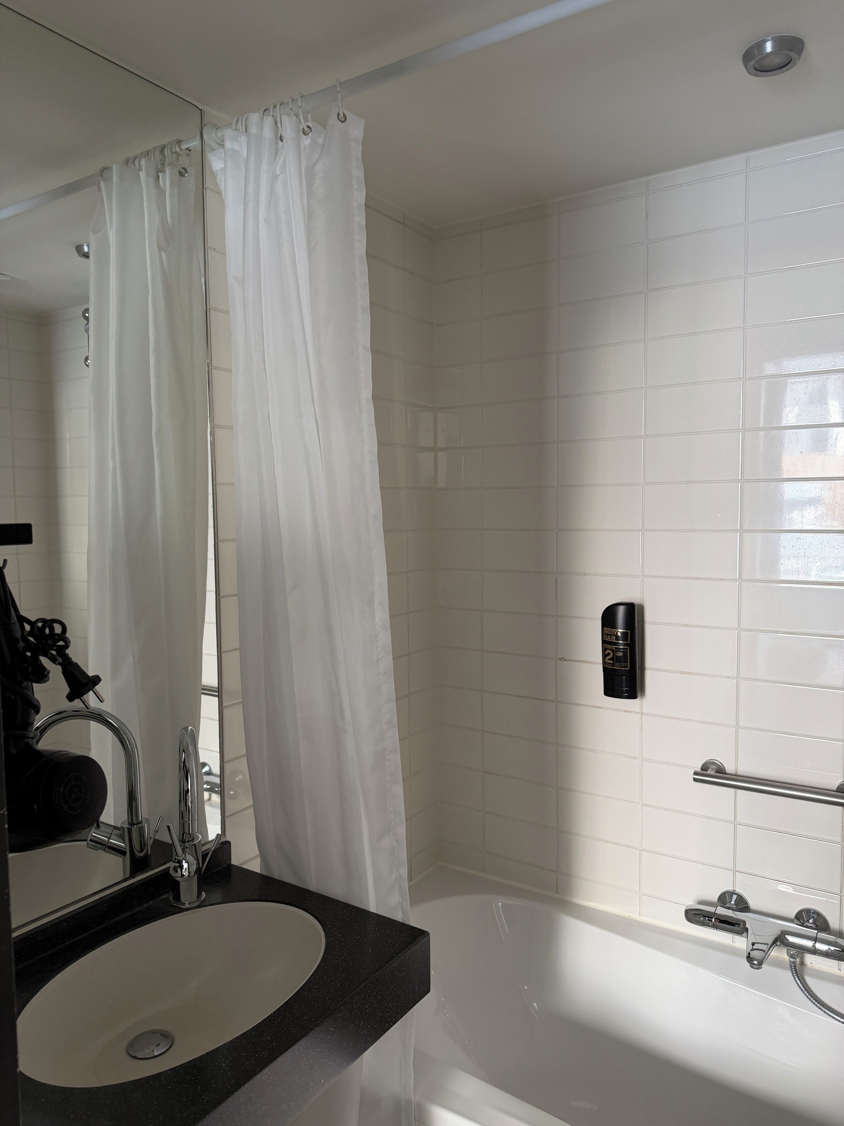 Une salle de bain avec une baignoire, un lavabo avec un miroir, un rideau de douche et un sèche-mains.