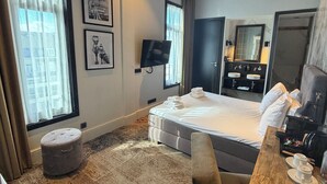 Ett hotellrum med en säng, ett skrivbord med en kaffebryggare, en TV och ett fönster med gardiner.