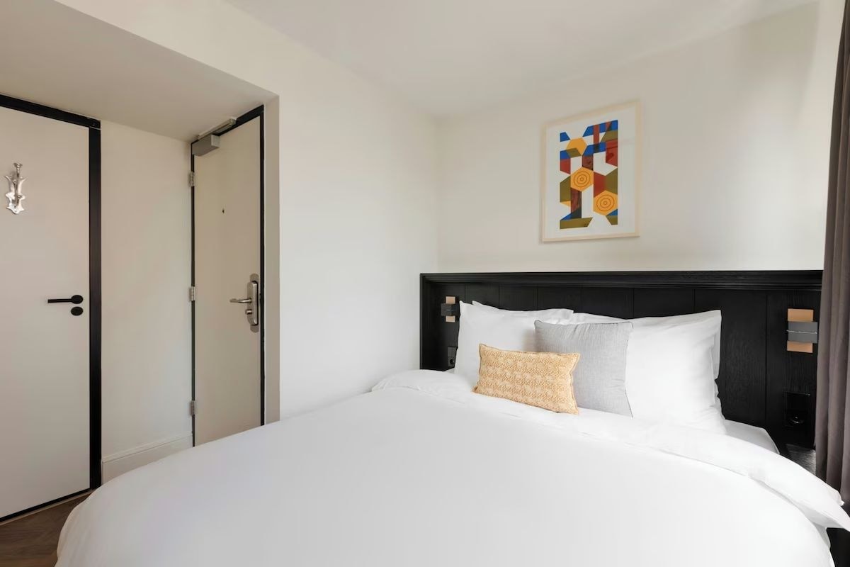 A hotel room with a large bed, a headboard, a door, and a wall-mounted artwork.