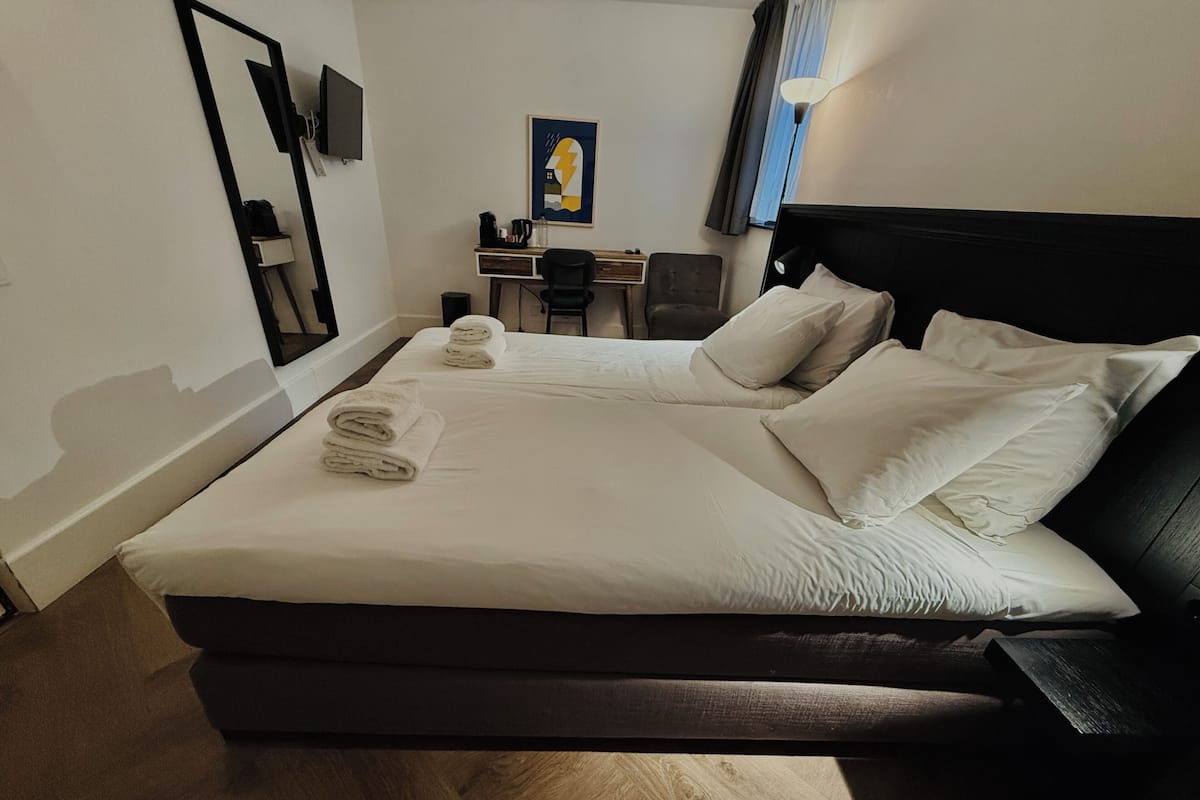Un lit bien fait, avec des oreillers et des serviettes, un bureau avec une chaise, une lampe et un tableau accroché au mur.
