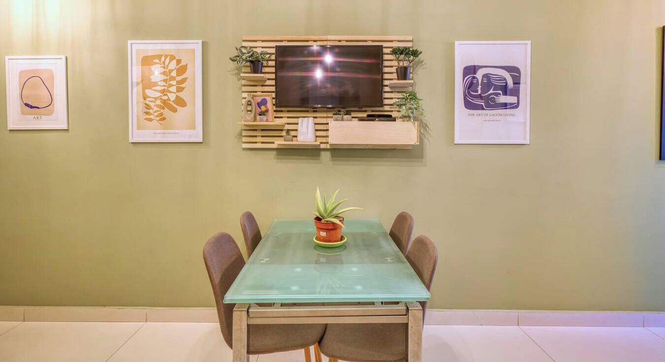A dining area with a glass table, six chairs, a potted plant, and a mounted TV.