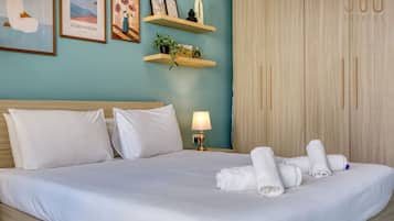Una cama bien hecha con sábanas blancas, una lámpara de noche y un juego de toallas sobre la cama.