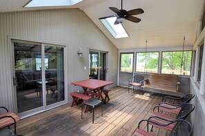 Eine überdachte Terrasse mit Tisch und Bänken, großen Schiebeglastüren und einem Deckenventilator.