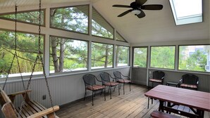 Een overdekte veranda met een schommel, houten stoelen, een tafel en een plafondventilator.