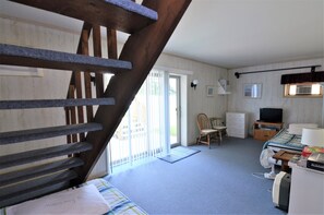 Ein Zimmer mit einer Holztreppe, einem Bett, einem Fernseher, einem Sessel und einem Schreibtisch mit einer Lampe.