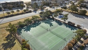 Luchtbeeld van een tennisbaan omgeven door woongebouwen, een weg en een strand.