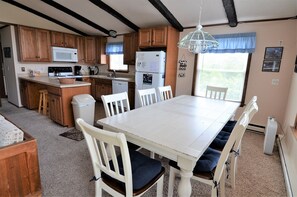 Eine Küche mit Holzausbau, einem weißen Herd und einem Kühlschrank. Ein Esstisch mit weißen Stühlen und blauen Kissen steht bereit.