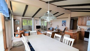 Een ruime keuken met een grote eettafel, houten keukenkastjes en een hangende lamp.