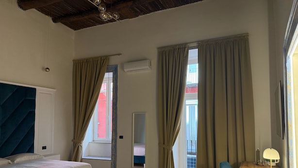 A bedroom with a bed, a desk with a lamp, and two windows with curtains. - Chiaia Lifestyle (Naples)