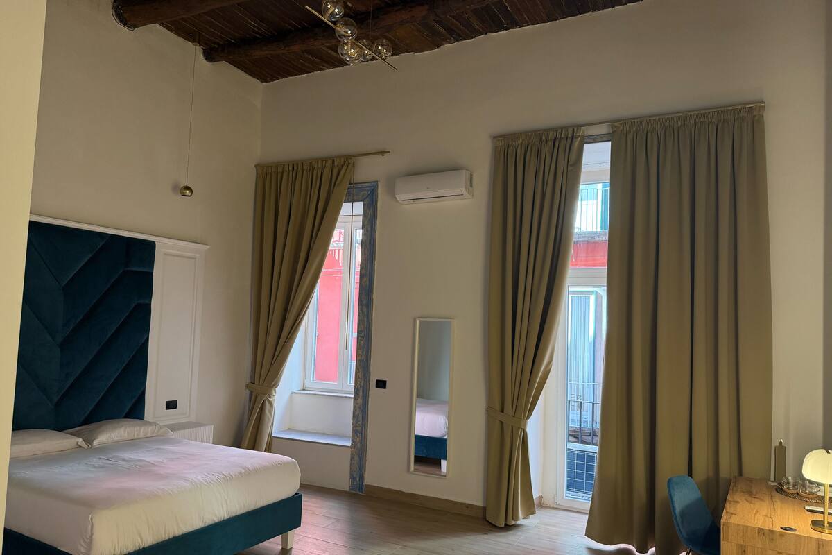 A bedroom with a bed, a wooden desk, and a window with curtains.