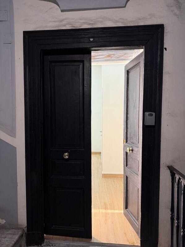 A black door leading to a room with wooden flooring and a white wall. - Chiaia Lifestyle (Naples)