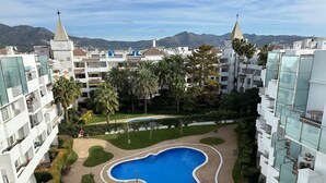 Un complexe résidentiel doté d’une piscine centrale, entourée de jardins bien entretenus et de palmiers.