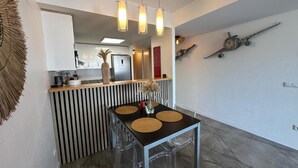 Une cuisine moderne dotée d’un îlot central, d’un éclairage suspendu et d’un coin repas avec une table et des chaises au design épuré.