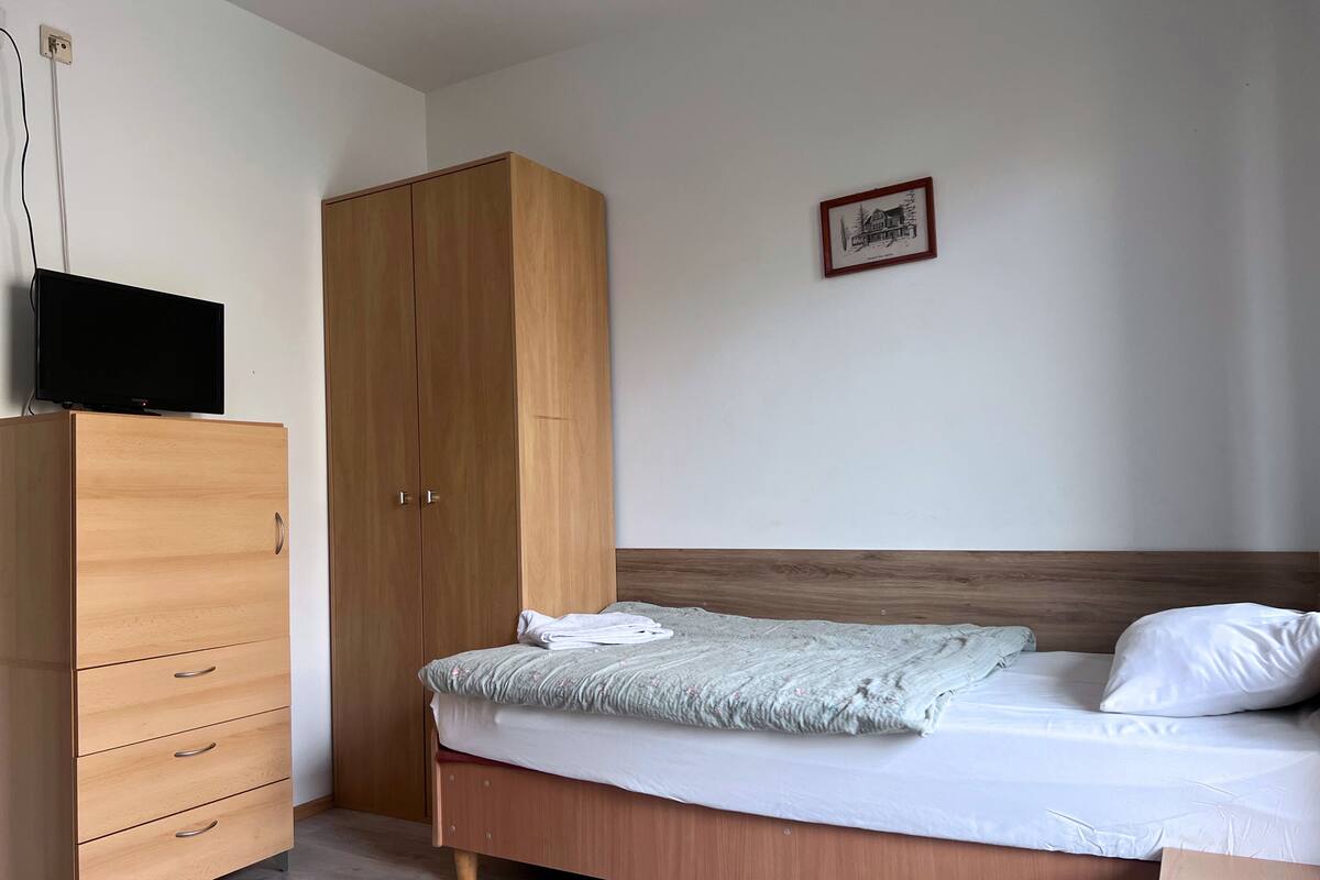 A bedroom with a wooden bed, a wooden wardrobe, and a television on top of the wardrobe.