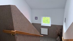 Eine Treppe mit Holzhandlauf, einem Heizkörper, einem Fenster mit Blick ins Grüne und einem Wandbild.