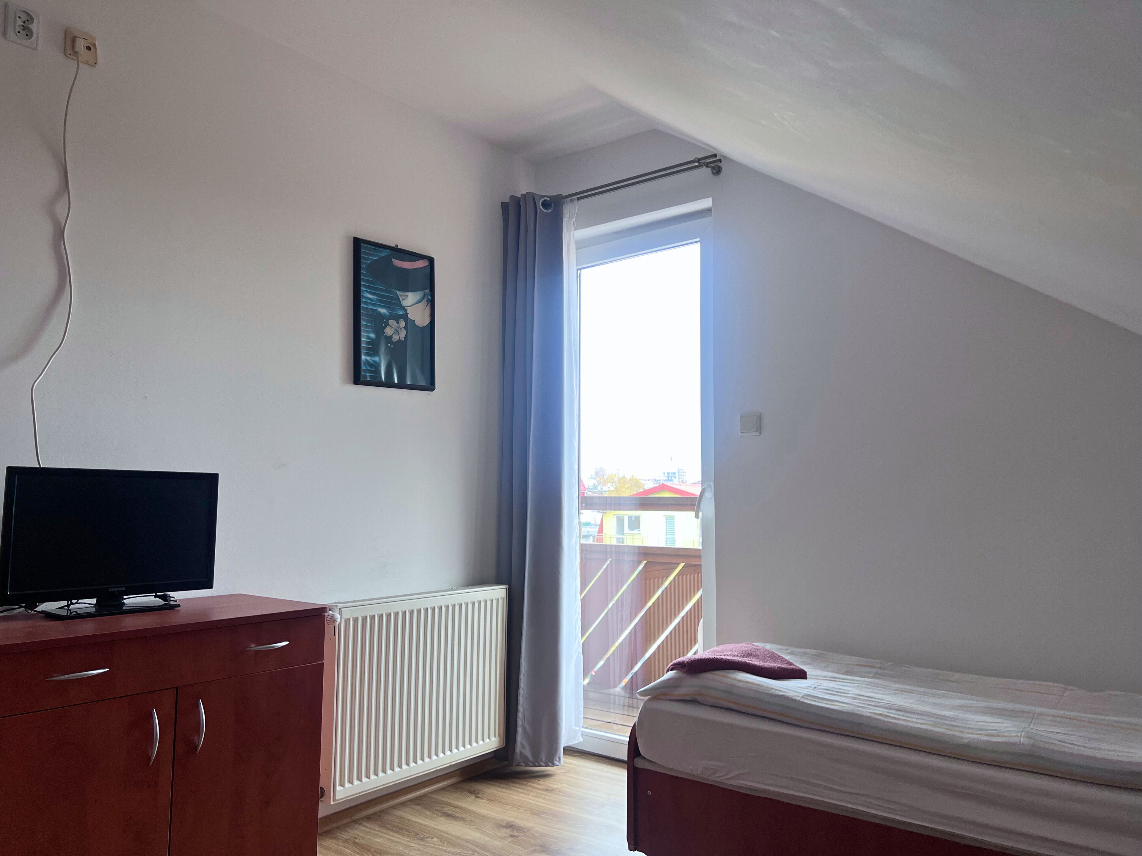 A bedroom with a bed, a dresser, a radiator, a window with curtains, and a painting on the wall.