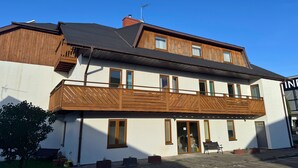 Ein zweistöckiges Gebäude mit einem hölzernen Balkon, großen Fenstern und einem sichtbaren Schornstein.