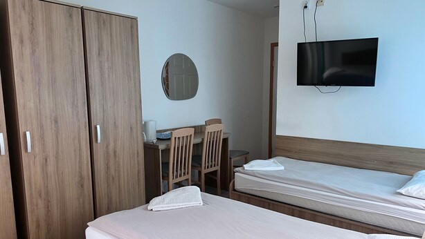 Ein Hotelzimmer mit zwei Betten, einem Schreibtisch mit Stuhl, einem an der Wand befestigten Fernseher und einem Kleiderschrank.