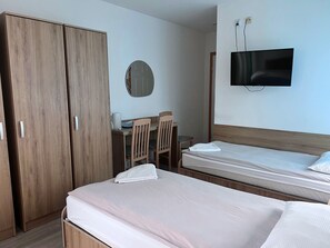 Ein Hotelzimmer mit zwei Betten, einem Schreibtisch mit Stuhl, einem an der Wand befestigten Fernseher und einem Kleiderschrank.