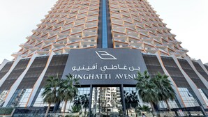 A modern building with a unique triangular facade, featuring balconies and a central entrance. - Modern 1BR with Pool and Gym Al Jaddaf (Dubai)