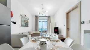 A modern hotel room with a dining area, a sofa set, a flat-screen TV, and a view of the city. - Modern 1BR with Pool and Gym Al Jaddaf (Dubai)