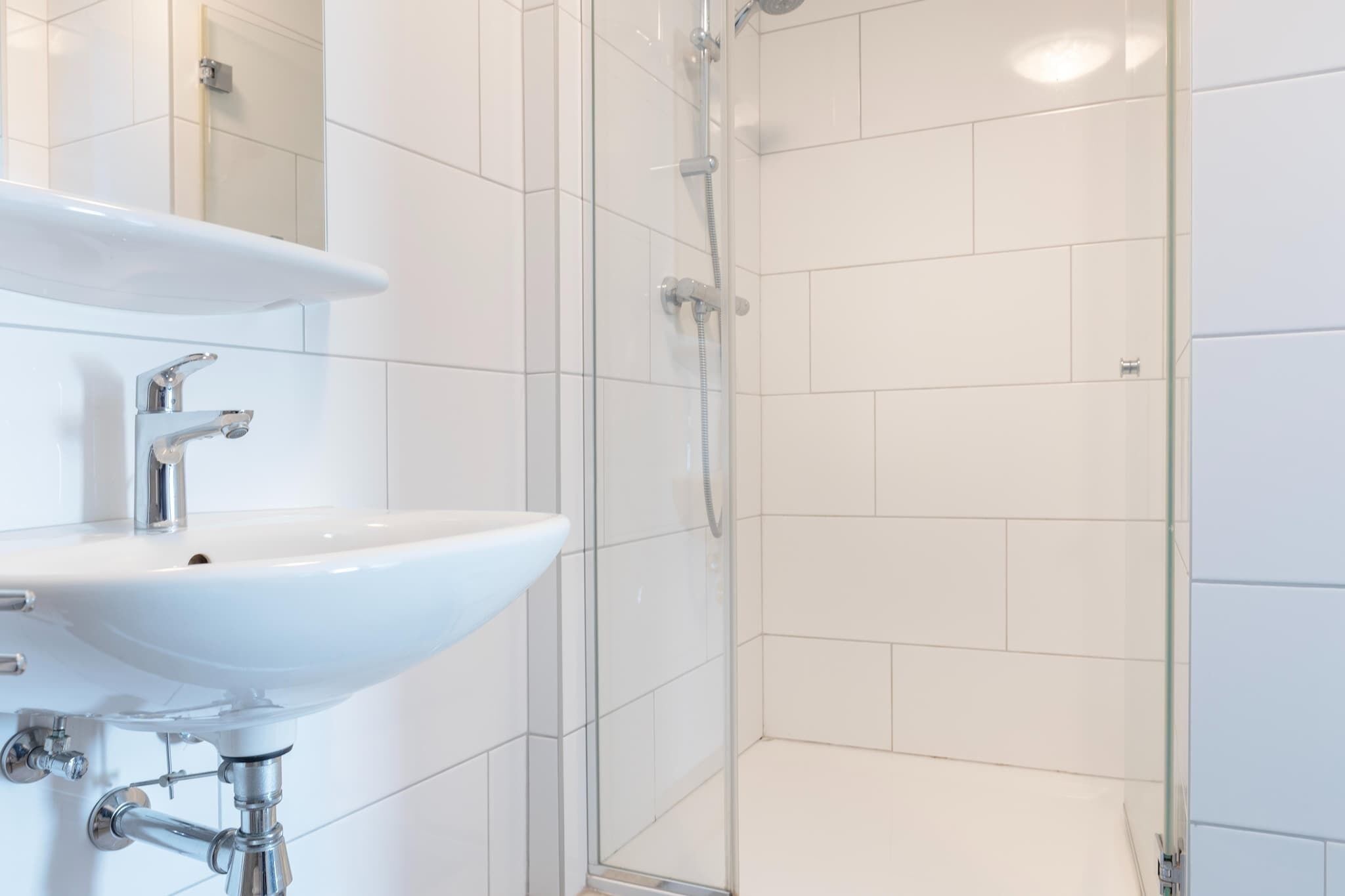 Une salle de bain moderne avec un lavabo blanc, un miroir et une douche en verre.