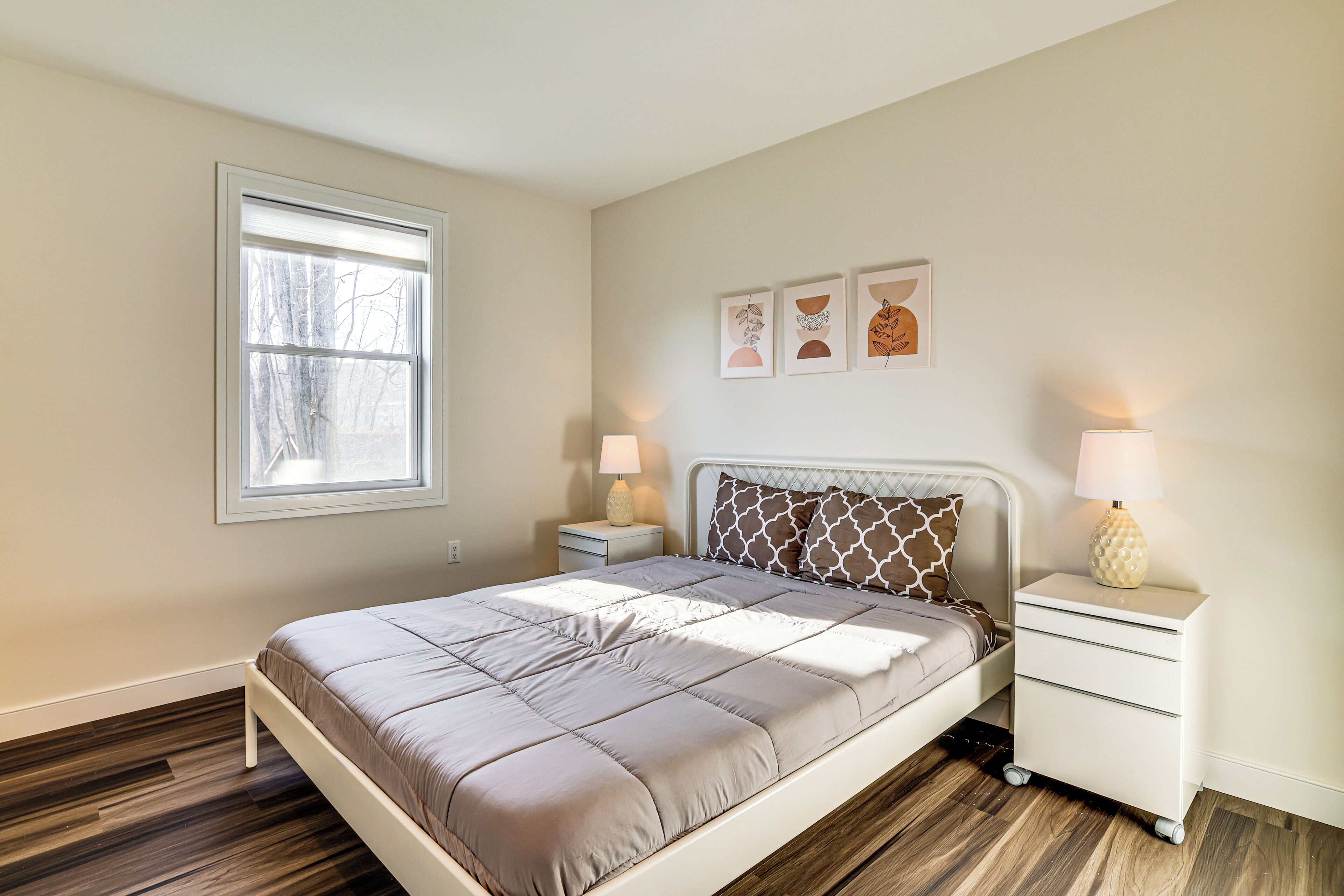 A bedroom with a bed, bedside tables, a window, and wall art.